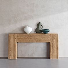 two vases sit on top of a wooden table in front of a white wall