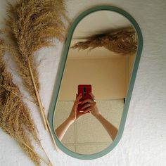 a person taking a selfie in front of a mirror with some dried grass on the floor