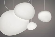 three white balls hanging from strings on a gray background with one ball suspended above the other