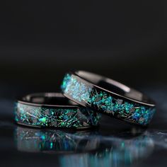 two wedding rings with green and blue glitters on the inside are shown in front of a black background