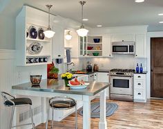 a kitchen with white cabinets and stainless steel appliances, including a center island in between two bar stools