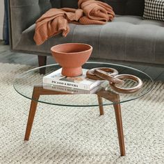 a glass table topped with a book and a bowl on top of it next to a couch