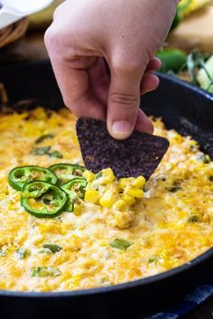 a person dipping a tortilla chip into a skillet with corn and jalapenos