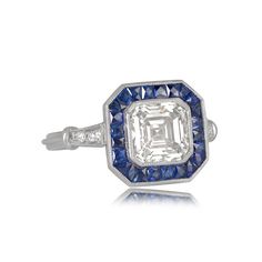 This geoemtrically designed engagement ring features a 2.01 carat asscher cut diamond with J color and VS2 clarity. Surrounding the center diamond is a halo of natural calibre French-cut sapphires with a vibrant blue saturation. The triple wire shank leads to accenting stones on either shoulder, with beautiful a openwork filigree under-gallery. ✦ DIAMOND SPECIFICATIONS: Diamond Cut: Asscher Cut Diamond Clarity: VS2 Diamond Color: J Color Diamond Weight 2.01 Carats ✦ ENGAGEMENT RING SPECIFICATION Gia Certified Cushion Cut Sapphire Ring In Platinum, Classic Octagon Sapphire Ring With Diamond, Luxury Gia Certified Octagon Sapphire Ring, Gia Certified Octagon Sapphire Luxury Ring, Gia Certified Octagon Sapphire Ring, Luxury Style, Octagon Brilliant Cut Sapphire Ring With Diamond, Luxury Gia Certified White Sapphire Ring, Luxury Octagon Sapphire Ring With Center Stone, Luxury Octagon Sapphire Ring With Brilliant Cut