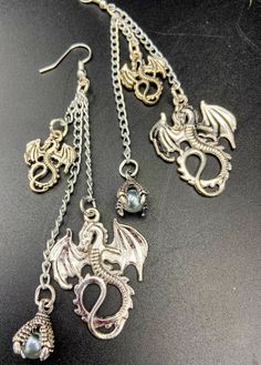 Unique and unusual dragon charm earrings. Adorned with gothic dragon charms and a glass pearl in a dragons talons. There are lightweight earrings which are nickel free and silver plated. They are about 4 inches long. These make a great gift idea! Punk Metal Jewelry For Fantasy Events, Fantasy Metal Single Earring, Fantasy Style Metal Single Earring, Fantasy Dangle Earrings For Halloween, Fantasy Metal Earrings For Halloween, Halloween Fantasy Dangle Earrings, Fantasy Halloween Dangle Earrings, Halloween Fantasy Dangle Jewelry, Fantasy Halloween Dangle Jewelry