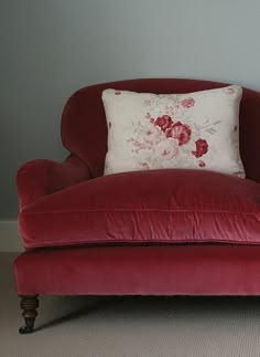 a red chair with a floral pillow on it's back in front of a gray wall