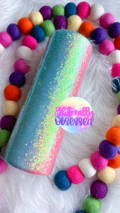 a blue tube with rainbow glitter on it surrounded by pom - poms and beads