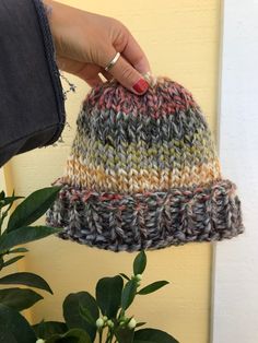 a woman's hand holding onto a multicolored knitted hat