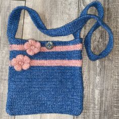 a crocheted blue purse with pink flowers on the front and side, sitting on a wooden floor