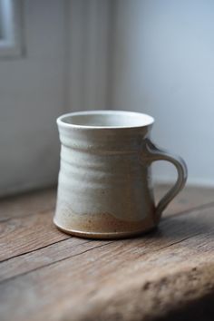 a white coffee cup sitting on top of a wooden table next to an open window