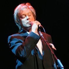 a man in a suit holding a microphone up to his face while standing on stage