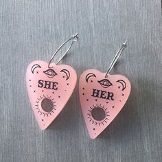 Be your most authentic, spooky you and share your pronouns with the world with these pronoun planchette earrings. If you would like to mix and match, choose the custom option and let us know what pronouns you want in the notes section of your order. Have sensitive ears? No problem, we've got you covered with options of Sterling Silver posts, Hypoallergenic Stainless Steel Posts, or Stainless Steel Hoops. Planchette measures 1.5in long and 1in wide. Handmade Edgy Plug Earrings As Gift, Handmade Edgy Plug Earrings For Gift, Edgy Nickel-free Earrings For Gift, Edgy Pink Jewelry For Gifts, Edgy Pink Jewelry For Gift, Edgy Nickel-free Plug Earrings As Gift, Nickel Free Edgy Plug Earrings As Gift, Handmade Edgy Earrings For Festivals, Punk Heart-shaped Earrings For Gifts