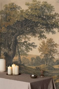 two candles are sitting on a table in front of a wall mural