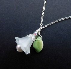 "Fresh as a bright Spring day, is this white lucite flower pendant necklace with it's jaunty leaf, and Silver-plated findings.  Frilly layered flowers with a White Swarovski pearl peeping out, and green glass leaf wire-wrapped beside it, are hung from a delicate Silver-plated chain. Two frosted white lucite ruffled lily flowers are layered together with the 6mm pearl.  The flowers are capped with a pointed 'petal' bead cap, and a 3mm Czech fire-polished crystal in Aurora Borealis. A small green Delicate Green Sterling Silver Necklaces, Green Flower Pendant Jewelry For Wedding, Green Flower Pendant Necklace For Wedding, Delicate Green Sterling Silver Necklace, White Flower-shaped Necklace With Pearl Pendant, White Flower-shaped Pearl Pendant Necklace, Delicate Green Necklace For Wedding, White Flower-shaped Sterling Silver Necklace, White Sterling Silver Flower Necklace