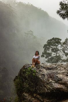 a woman sitting on the edge of a cliff