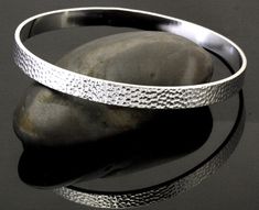 All of our endless bangles start as high quality jeweler's brass seamless rings which we hand emboss, one at a time. Each piece is then finished with a high grade silver plate. They are extremely durable and will retain their beauty for years. Silver Hammered Metal Bangle, Silver Hammered Round Bangle, Hammered Silver Round Bangle, Handmade Metal Bangle For Anniversary, Silver Hammered Bangle Bracelet, Silver Hammered Bangle Jewelry, Hammered Sterling Silver Round Bangle, Adjustable Etched Round Bangle, Hammered Sterling Silver Bangle