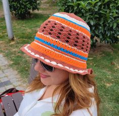 a woman wearing a crocheted hat and sunglasses sitting on a bench in the park