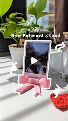 a photo frame with a pink bow on it next to a vase and potted plant