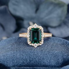 an emerald and diamond ring sitting on top of a blue velvet cushion with flowers in the background