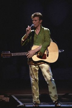 a man holding a guitar while standing on top of a stage in front of a microphone