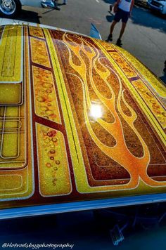 the hood of a classic car with flames painted on it and people walking in the background