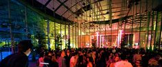 a large group of people standing in a room with lights on the ceiling and windows