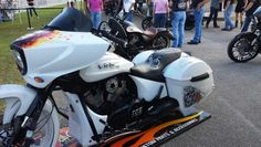 several motorcycles are parked on the side of the road with people looking at them in the background