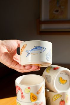 a person holding a cup in front of three cups with fish designs on the sides