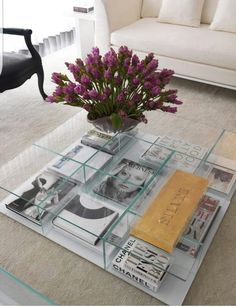 a glass coffee table topped with magazines and flowers