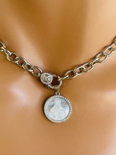 This is a beautiful 14k white gold filled chain choker necklace with mother of pearl etched miraculous Mary pendant hanging from front pave lobster clasp. These beautiful pendant measures 18 mm. features the miraculous image of MARY surrounded with pavé crystals. Necklace chain links measure 10 X7MM. Clasp sits at front that holds pendant. This necklace is also available in 14k gold filled.  Model has a small neck and is wearing a 15 inch length. Please choose your desired length. Comes in a gift box ready to present. Please choose the length and primary color. Catholic Jewelry Necklace, Pearl Charm Necklace, Crystals Necklace, Catholic Jewelry, Pendant Choker, Charm Necklace Silver, Chain Links, Catholic Gifts, Chain Choker Necklace