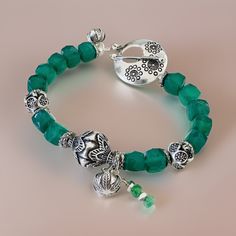 Discover the allure of this Bohemian style natural stone bracelet, featuring 8mm natural green Onyx cube stones that dazzle with their stunning translucent green hue and sparkling facets. At its heart lies a 12mm ornate Karen Hill Tribe Silver focal bead, accompanied by a charming Karen Hill Tribe Silver leaf pattern ball charm and a green Onyx charm delicately dangling on the side. The bracelet is adorned with Karen Hill Tribe Silver beads and spacer beads, meticulously oxidized to reveal mesmerizing pattern details. Completing the look is a large flower-stamped Karen Hill Tribe Silver toggle clasp and another Karen Hill Tribe Silver leaf pattern ball charm with a total length of 7 3/4 inches.  This unique Onyx bracelet is not just a piece of jewelry--it's a symbol of peace, purity, and m Adjustable Faceted Crystal Bohemian Bracelet, Bohemian Adjustable Faceted Crystal Bracelet, Adjustable Faceted Bohemian Crystal Bracelet, Bohemian Silver Faceted Beaded Bracelets, Bohemian Jade Crystal Bracelet With Gemstone Beads, Bohemian Jade Crystal Bracelet With Natural Stones, Bohemian Jade Bracelets With Gemstone Beads, Bohemian Jade Bracelets, Bohemian Adjustable Jade Crystal Bracelet