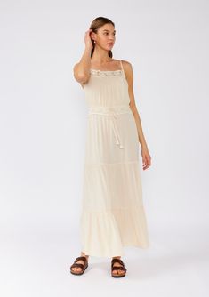 [Color: Natural] A front facing image of a brunette model wearing an off white sleeveless maxi dress. With adjustable spaghetti straps Spring Tiered Maxi Dress With Lace Trim, Summer Maxi Dress With Lace Trim And Tiered Skirt, Summer Tiered Maxi Dress With Lace Trim, Summer Tiered Maxi Dress In Rayon, Summer Rayon Tiered Maxi Dress, Casual Maxi Dress With Lace Trim, Vacation Maxi Dress With Lace Trim, Bohemian Tiered Dress With Adjustable Straps, Flowy Lace Trim Sundress Maxi Dress