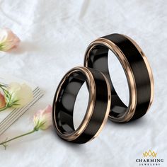 two black and gold wedding bands next to each other on a white sheet with flowers