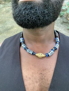 This fun necklace features blue recycled glass bead accenting hand painted recycled class beads made by the Krobo people of Ghana. These beads feature the Adinkra symbol, Gye Nyame, which speaks to the omnipotence of God. It also has a Boule brass centerpiece with coconut shells and a brass clasp. Length: 20 inches Unique Blue Wooden Beads, Blue Wooden Beads For Festival, Blue Wooden Beads, Unique Blue Wooden Beaded Necklaces, Artisan Blue Wooden Beads, Blue Wooden Beads Festival Jewelry, Blue Wooden Beads Jewelry For Festival, Unique Blue Jewelry With Black Beads, Unique Blue Jewelry With Wooden Beads