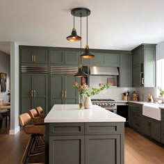 a large kitchen with green cabinets and white counter tops, along with an island in the middle