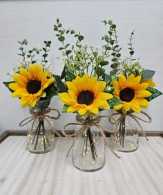 three vases with sunflowers and greenery tied to them on a table