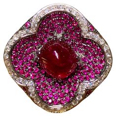 A contemporary gemstone cocktail ring crafted in 18K white gold centered by a 1.03ct natural cabochon sugarloaf cut vividly red ruby (heat only) surrounded by another 4.65cttw in natural rubies as well as 1.23cttw in G-I color Vs1-Si1 clarity round diamonds. All stone weights are stamped and exact. Dimensions/Weight: Ring measures 1” diameter and weighs 11.5g. Size 7. Condition: All stones are secure and in perfectly wearable condition. R-ANYEH Luxury Red Cabochon Ruby Ring, Fine Jewelry Red Cabochon Ruby Ring, Turquoise Diamond Rings, Cocktail Jewelry, White Gold Sapphire, White Gold Set, Chevron Ring, Diamond Cocktail Rings, Ruby Stone