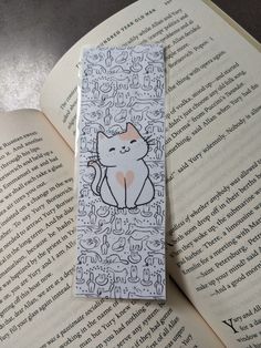 a bookmark with an image of a cat sitting on it's side in front of an open book