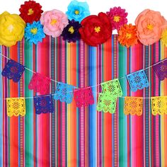 colorful paper flowers are hanging from a string on a striped background with rainbow colored ribbons