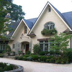 a white house with lots of windows and plants in the front yard, surrounded by greenery