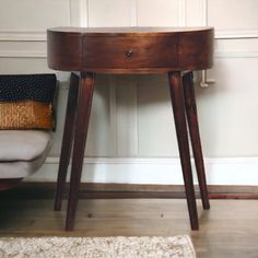 a small wooden table sitting next to a chair in a room with white walls and wood flooring