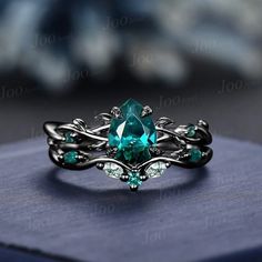 a ring with an oval cut green stone surrounded by vines and leaves, on top of a blue box