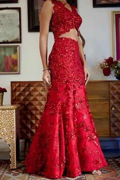 This structured red mermaid lehenga set personifies the emblem of romantic glamour. The set features intricate embroidery of cutdana work and dori with red sequins, beads, and floral applique work adorning both the skirt and blouse. Its focal point is the tassel detailing flowing at the bottom of the skirt with cute flower motifs made of sequins. • Sleeveless blouse with floral applique detailing highlighted with nalki crystals and beads.• Blouse contains a metal hook on the front side.• Heavily embroidered dupatta with botanical motifs detailing accentuated with sparkling sequins and crystals. • Lehenga skirt adorned with floral applique handwork detailing and drop-down tassels adorning the bottom of the skirt. • Lehenga contains a left zipper for support along with a metal hook.From Mole Red Floor-length Sharara For Reception, Red Sharara With Floral Embroidery For Wedding, Elegant Red Sharara With Floral Embroidery, Fitted Floral Embroidered Evening Sharara, Festive Embroidered Evening Dress For Reception, Red Floor-length Choli With Sequins, Elegant Red Lehenga With Sequins, Red Sequined Floor-length Choli, Festive Evening Dress With Resham Embroidery