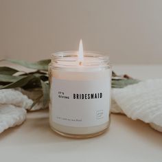 a white candle sitting on top of a table next to some towels and leaves with the words it's divine, bridesmaid