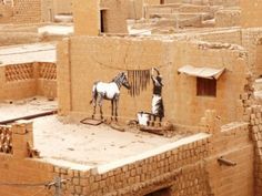 a man standing next to a white horse on top of a stone building in the desert