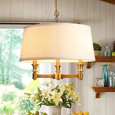 a lamp hanging over a table with fruit and flowers on the table next to it