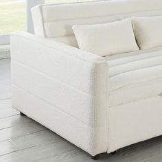 a white couch sitting on top of a hard wood floor next to a large window