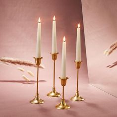 four candles are lined up on a pink surface with feathers flying in the air behind them