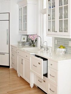 a kitchen with white cabinets and wood flooring next to a window filled with flowers