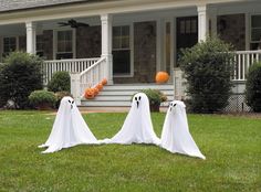 a group of ghost statues in front of a house with pumpkins on the lawn